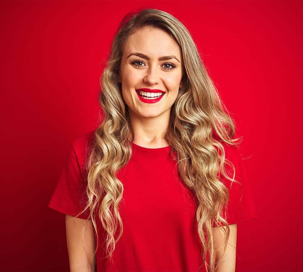 Young beautiful woman wearing basic t-shirt standing over red isolated background with a happy and cool smile on face.